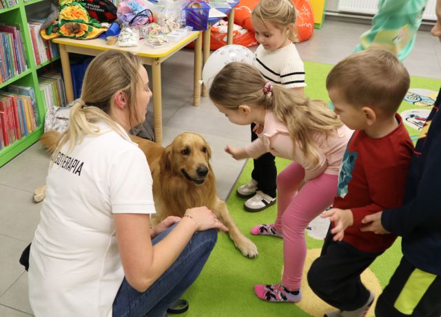 dzieci głaszą psa, obok kuca terapeutka