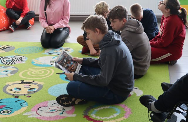 młodzież siedzi na dywanie, chłopiec czyta książkę