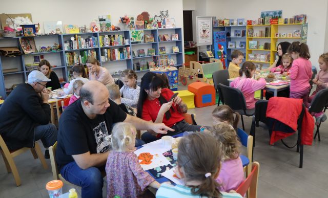 dzieci i rodzice siedzą przy stołach i lepią z modeliny