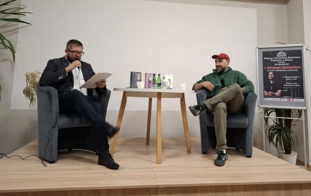 dwóch mężczyzn siedzący na krzesłąch przy okrągłym stole