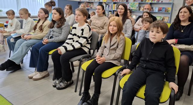 dzieci i rodzice siedzą na krzesłąch w bibliotece