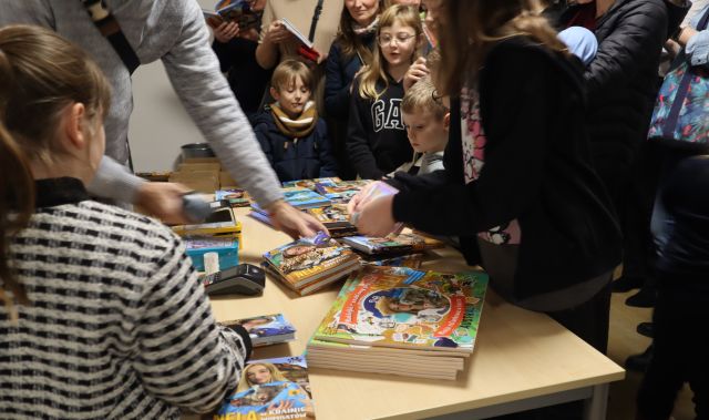 dzieci i dorośli zgromadzeni przy stoliku z książkami