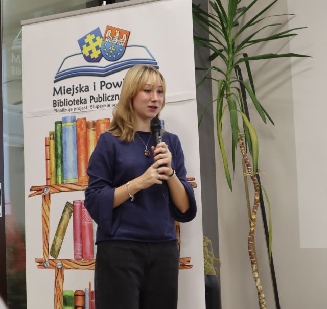 dziewczyna z mikrofonem, w tle baner biblioteki