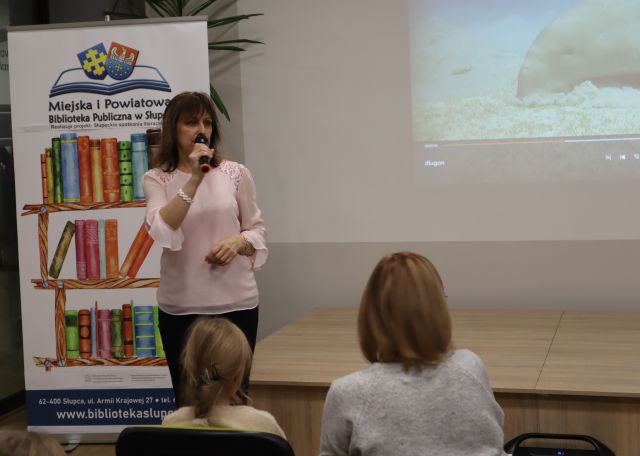 kobieta z mikrofonem, przed nią siedzą uczestnicy spotkania