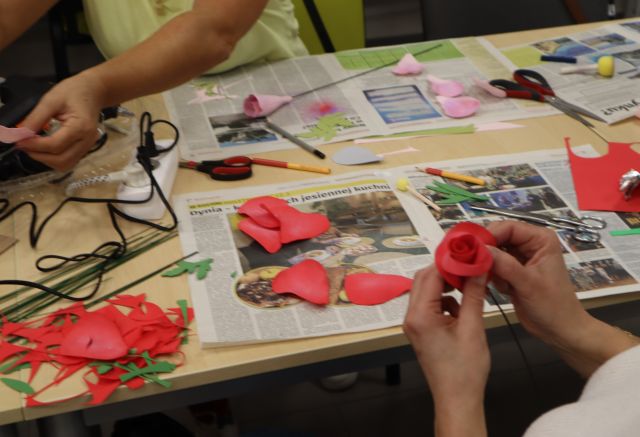 dłoń trzymająca różę z materiału, na stole wycięte płatki