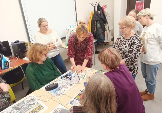 kobieta zawija gazetę na rorkę, inne kobiety przyglądają się