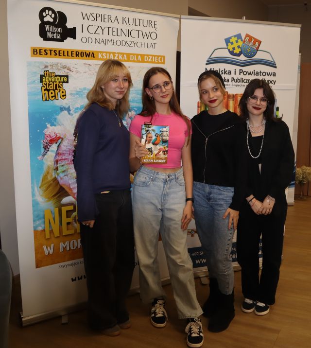 3 dziewczyny pozują do zdjęcia z Nelą na tle jej i biblioteki baneru