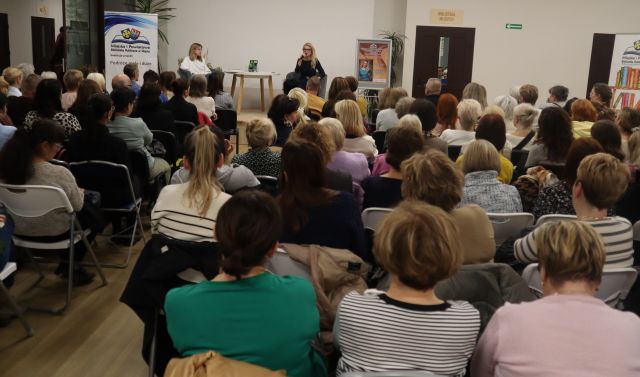 uczestnicy spotkania siedzący na krzesłach, przed nimi w tle siedzący na scenie pisarka i prowadząca spotkanie
