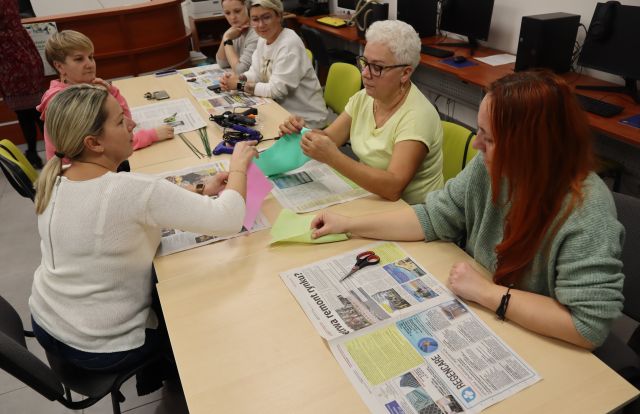 kobiety siedzą przy stolikach i wycinają z materiałów