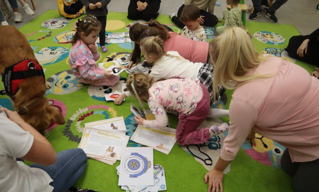 dzieci układają na dywanie obrazki, obok leży pies