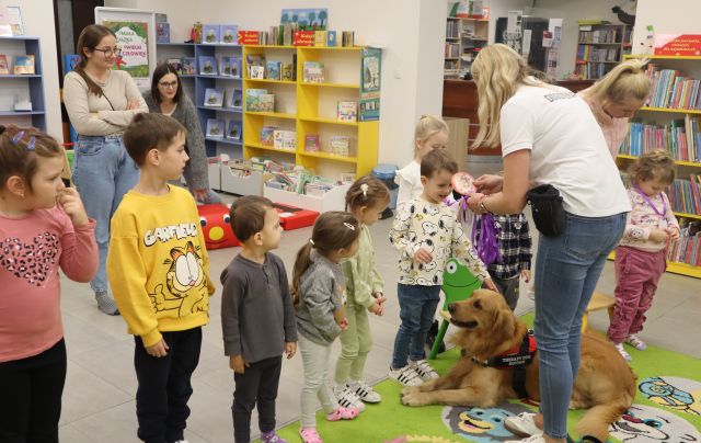 kobieta zakłada dzieciom na szyję medale z papieru, przed nimi leży pies