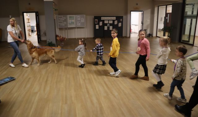 opiekunka prowadzi psa na smyczy, za nim idą dzieci trzymając się długiej smyczy