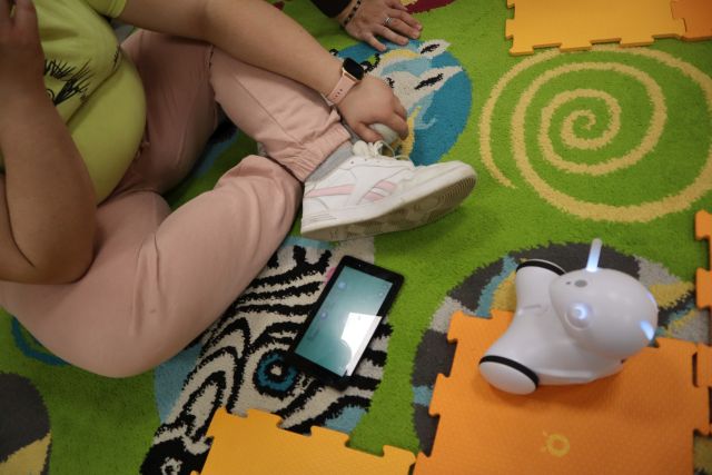 na kolorowym dywanie siedzi dziewczyna, obok niej leży tablet i robot Photon