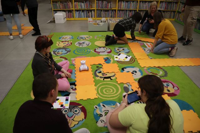 młodzież steruje robotami Photon, w tle regały z książkami