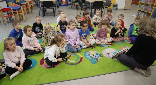 na kolorowym dywanie siedzą przedszkolaki i bibliotekarka z książkami