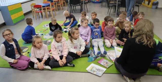 bibliotekarka czyta przedszkolakom siedzącym na kolorowym dywanie