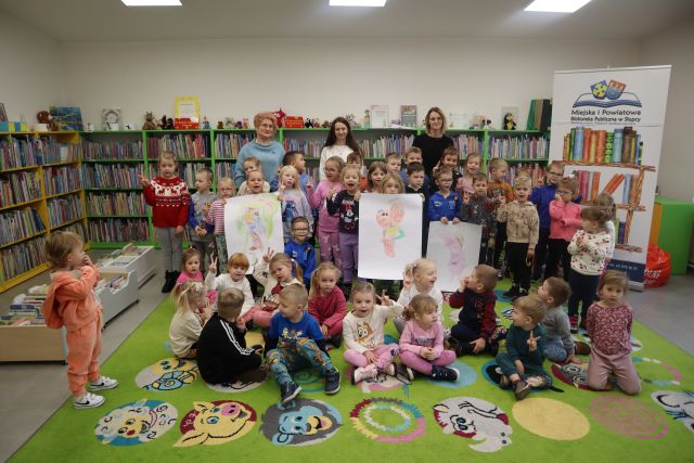 przedszkolaki i 3 nauczycielki pozują do zdjęcia, troje dzieci trzyma pokolorowane przez siebie postacie z bajek