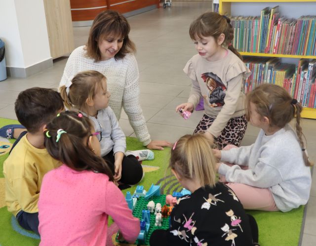 bibliotekarka siedzi przy układających puzzle dzieciach
