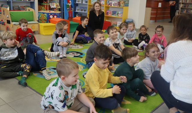 przedszkoalki siedzą na kolorowym dywanie przed dyrektorką biblioteki