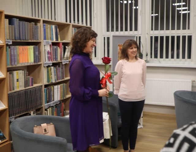 dwie kobiety stoją przed regałami z książkami, jedna z czerwoną różą