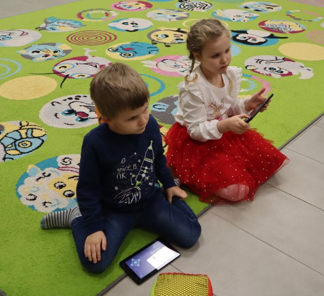 chłopiec i dziewczynka siedzą na dywanie, dziewczynka trzyma w rękach tablet