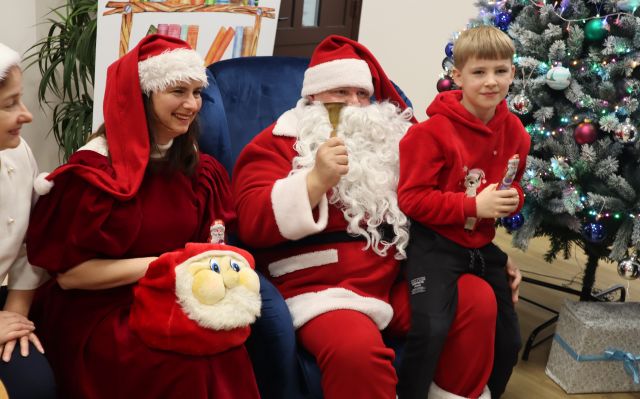 chłopiec siedzi na kolamach Mikołaja, obok siediz Mikołajowa