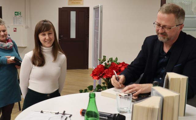 mężczyzna podpisuje książkę, obok stoi kobieta