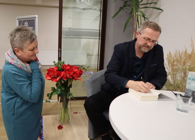 mężczyzna podpisuje książkę, obok stoi kobieta