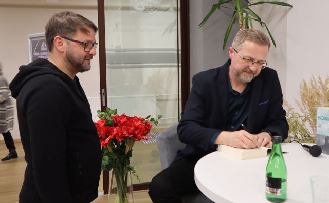 mężczyzna podpisuje książkę, obok stoi mężczyzna