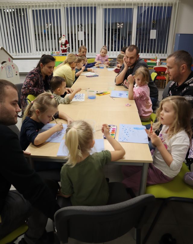 dzieci z rodzicami malują zimowe krajobrazy siedząc przy połączonych stołach