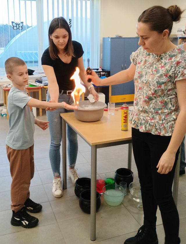 dwie kobiety podpalają na dłoni chłopca tworząc ogień