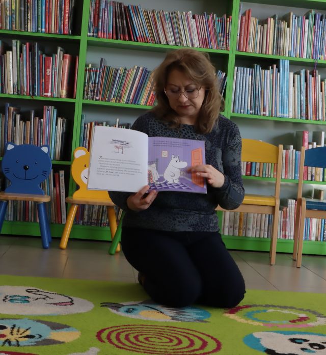 bibliotekarka pokazuje książkę, w tle regały z książkami