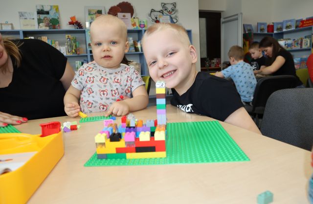 dwóch chłopców pozuje do zdjęcia, przed nimi na stole ułożona wieża z klocków LEGO