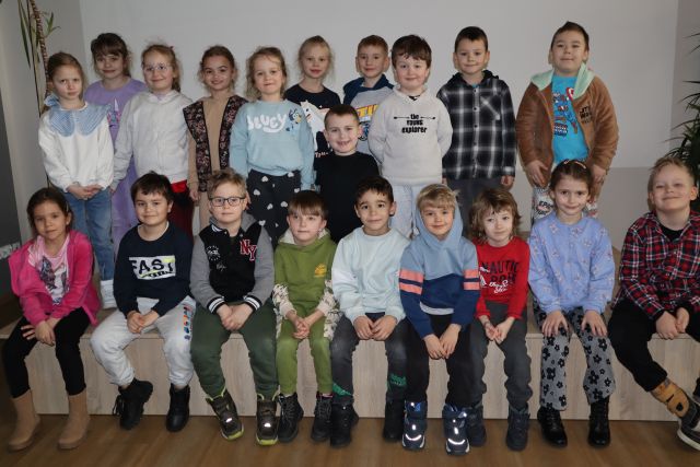 przedszkolaki stoją na podwyższenie i siedzą na scenie pozując do zdjęcia