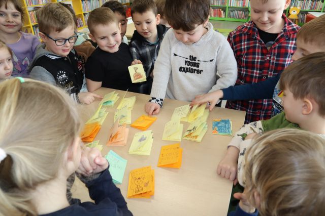 dzieci stoją przy stoliku z wyłożonymi małymi książeczkami zrobionymi przez dzieci z kartek