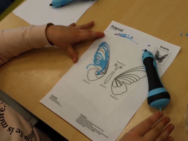 na zdjęciu dłonie dziecka i model motyla na kartce, jedno skrzydło pokryte niebieskim filamentem