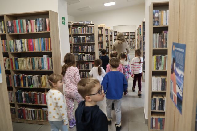 przedszkolaki w wypożyczalni dla dorosłych, na zdjęciu regały z książkami i dzieci
