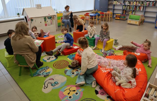 na pufach siedzą dzieci i bibliotekarka z książką
