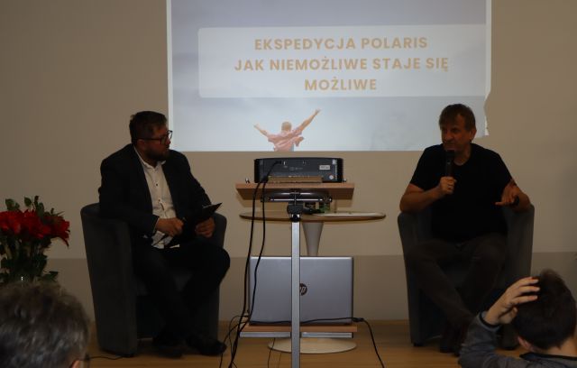 dwóch mężczyzn siedzi na fotekach na scenie, w tle prezentacja