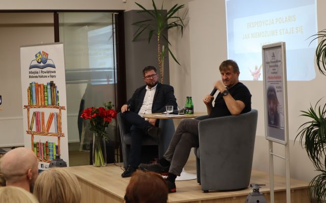 dwóch mężczyzn z mikrofonami na scenie siedzi w fotelach