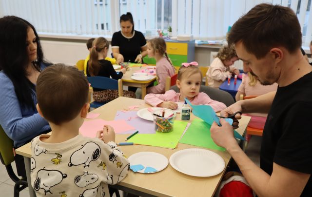 dzieci i rodzice siedzą przy stolikach, na których leżą papierowe talerzyki