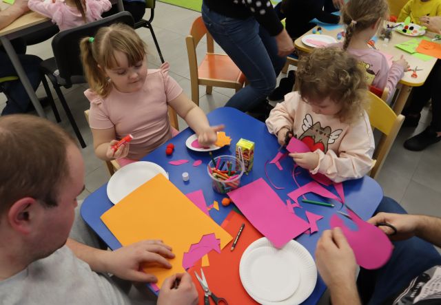 dzieci z rodzicami wycinają z kartek dinozaury