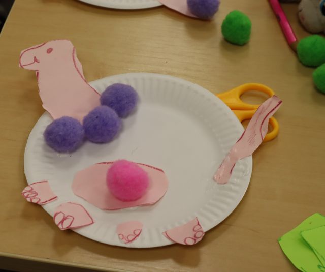 na papierowym talerzyku wycięty dinozar z kolorowymi kulkami z wełny