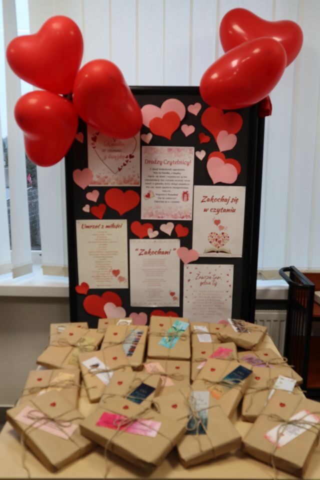 na zdjęciu tablica z cytatami z książek, serduszkami, wierszami miłosnymi, czerwonymi balonami sercami, na stole poukładane paczki ozdobione serduszkami i zakładkami do książek
