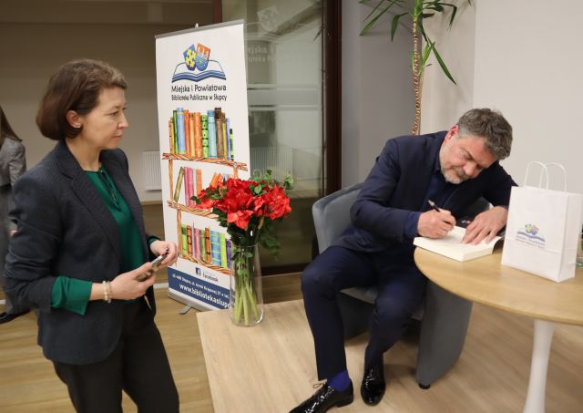 mężczyzna podpisuje książkę, obok stoi kobieta