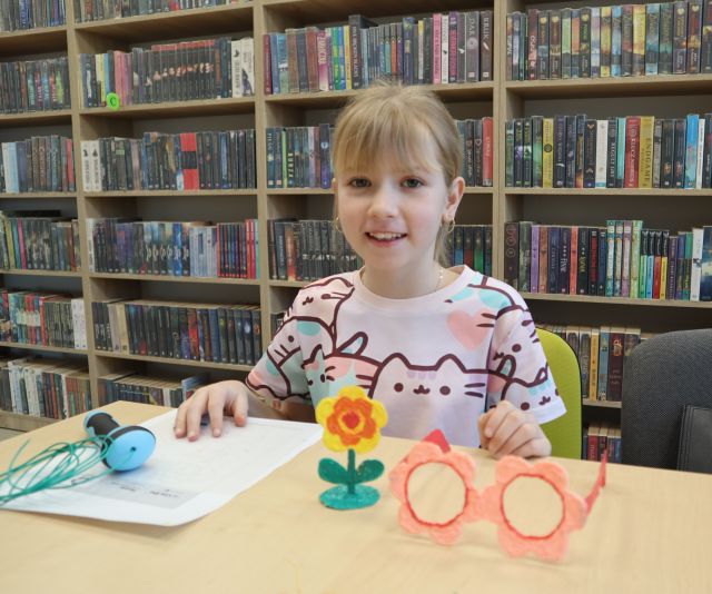 na zdjęciu uśmiechnięta dziewczynka, przed nią na stole kwiat i okulary 3D