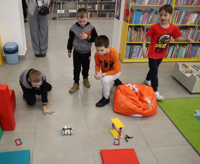 chłopcy sterujący robotem z klocków Lego, w tle regały z książkami
