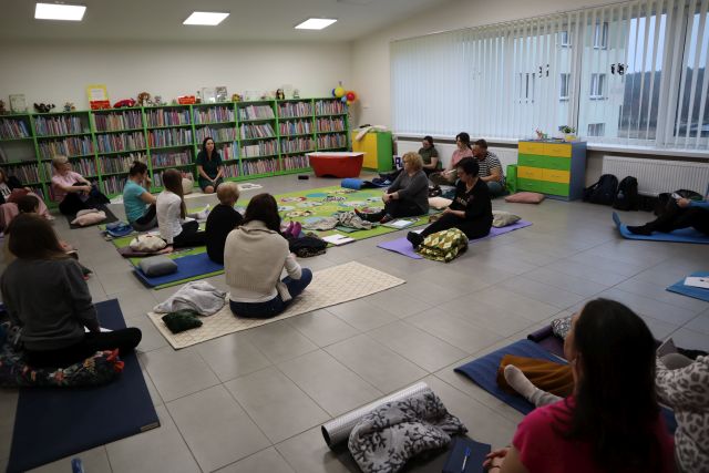 blisko 20 osób siedzi na karimatach, w tle regały z książkami