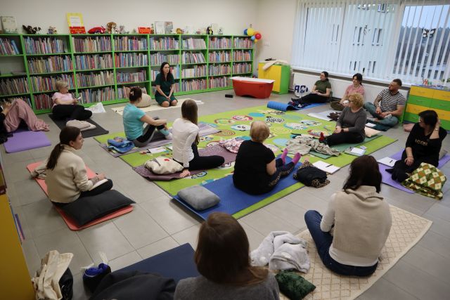 blisko 20 osób siedzi na karimatach, w tle regały z książkami