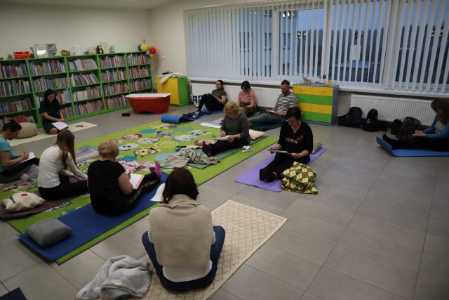 blisko 20 osób siedzi na karimatach, i notuje w notesach, w tle regały z książkami